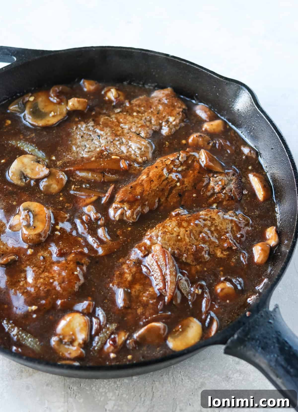 Effortless Tender Cube Steak 6 Cubed steak with mushroom and onion gravy in a 12-inch cast iron skillet, ready to be served.