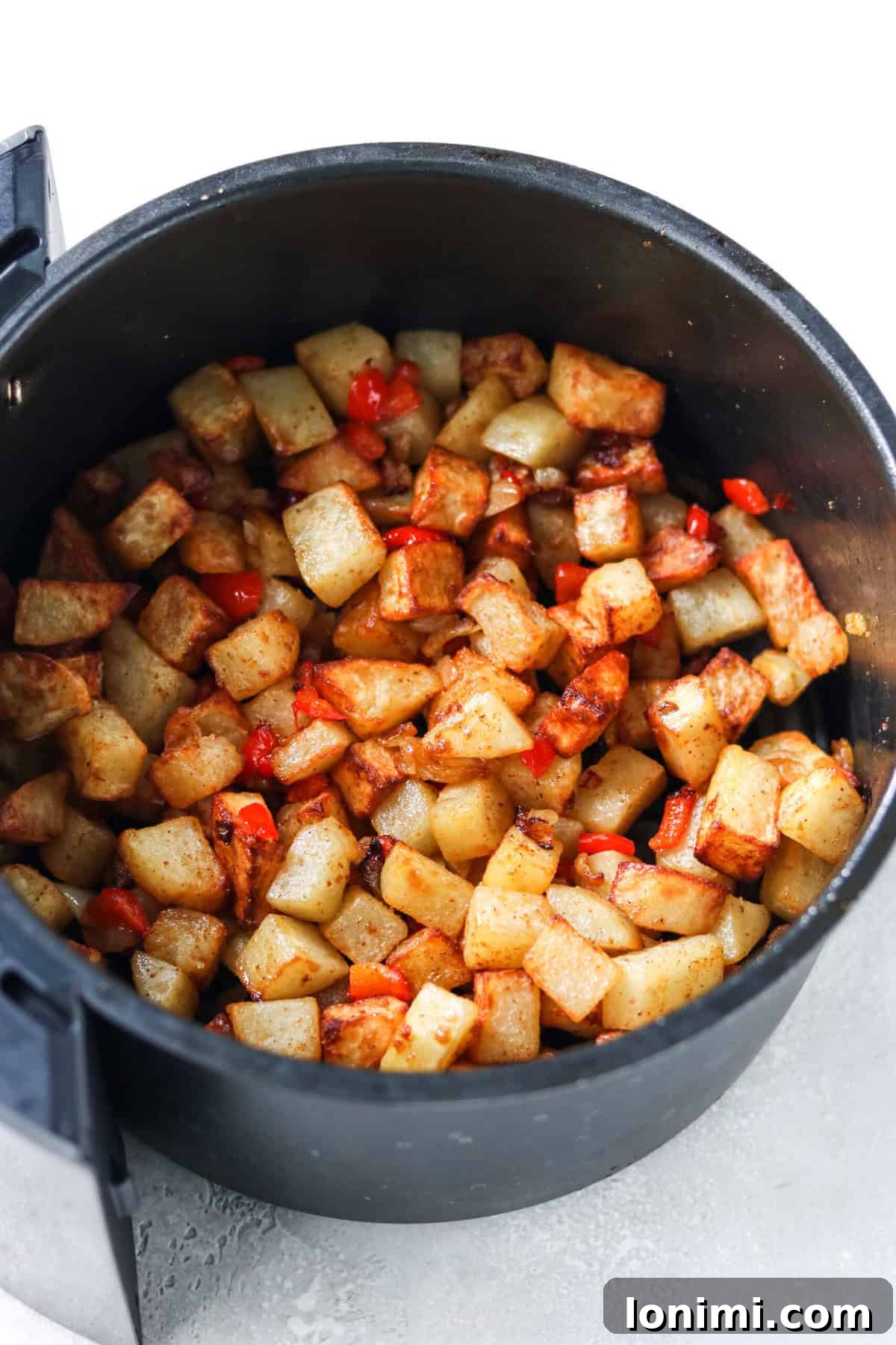 Cubed potatoes, bell pepper, and onion cooking in an air fryer basket.