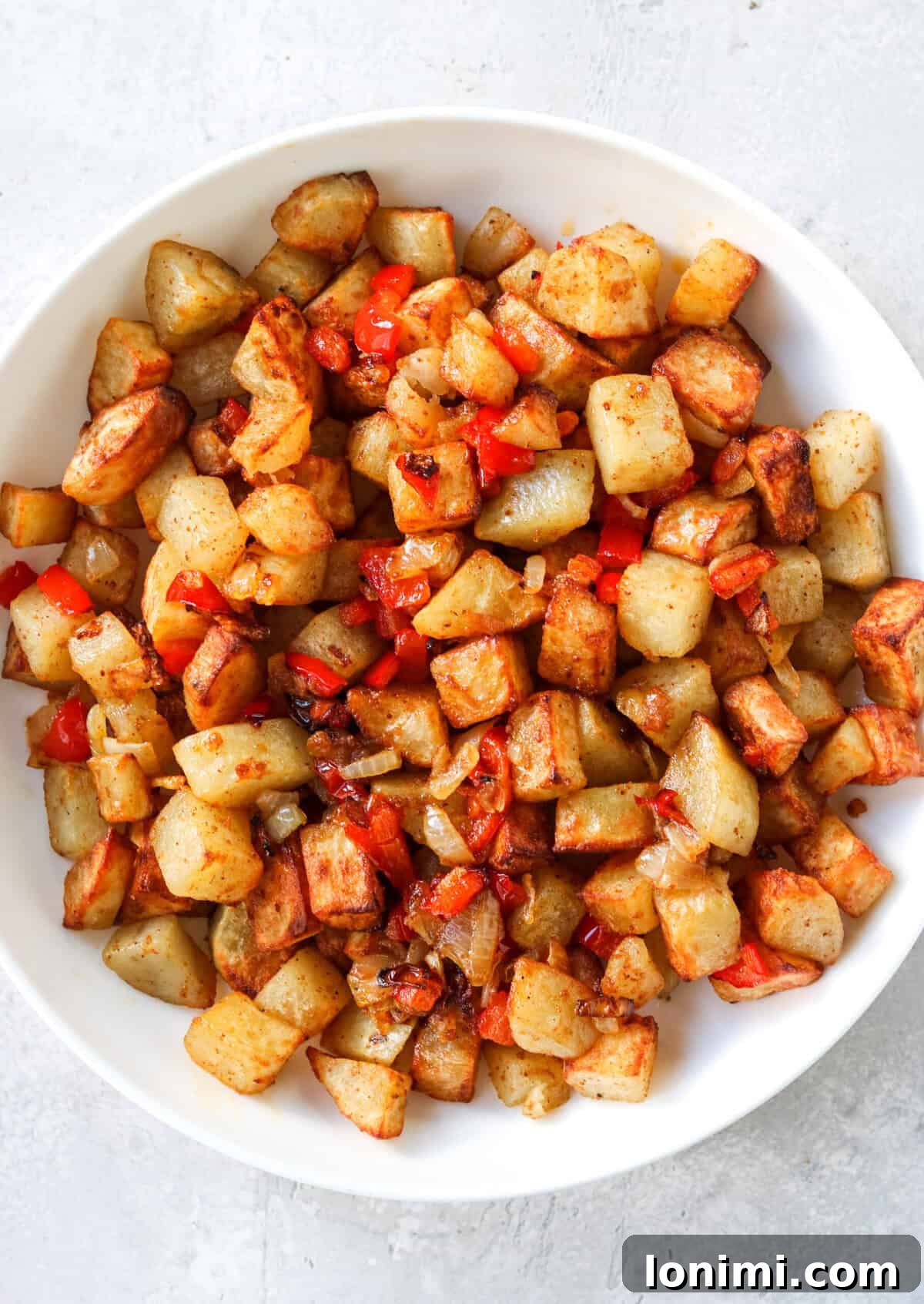A close-up photo of cubed potatoes with diced bell peppers and onions in a white bowl.