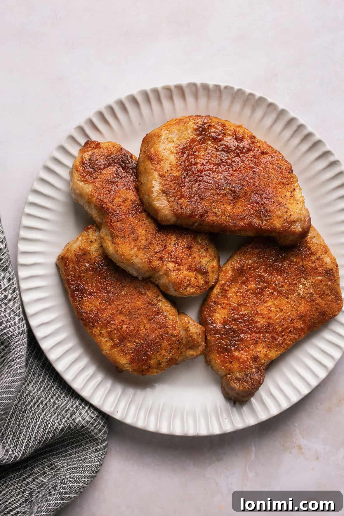 seasoned and cooked pork chops stacked on a white plate