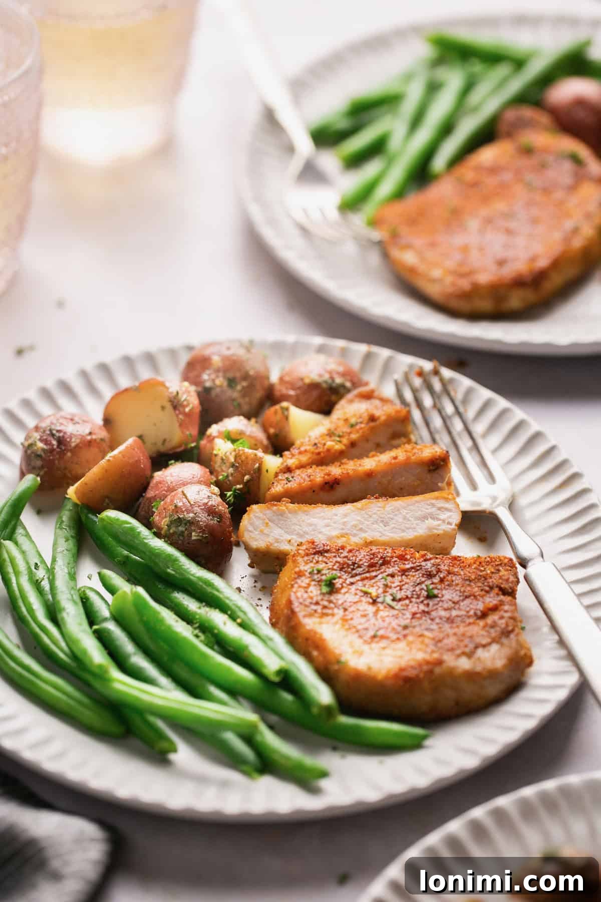 three white plates with potatoes, green beans, and slices of pork. 