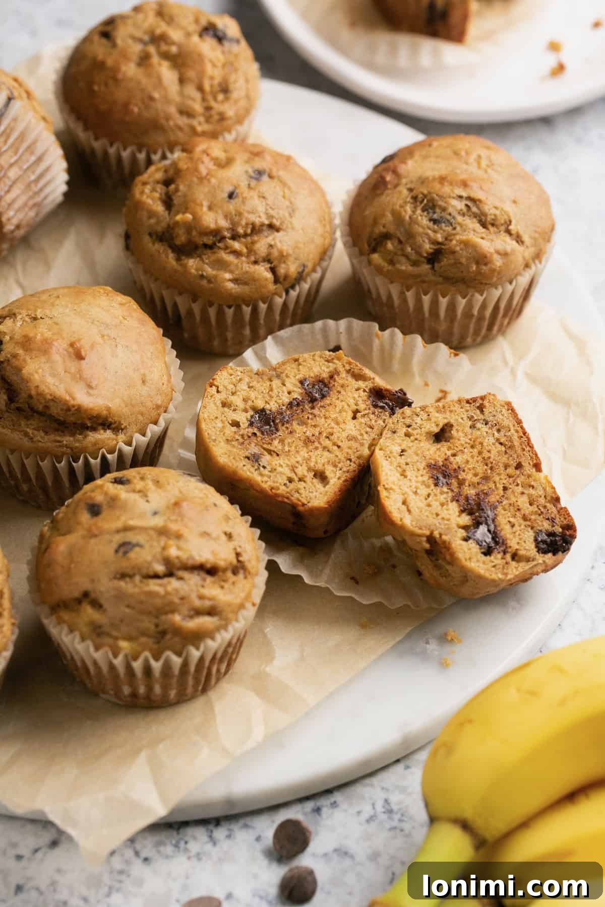 a close up shot of banana muffins wrapped in muffin lines with one sliced down the middle showing the inside