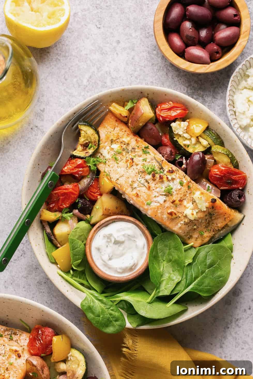 A bowl filled with fresh greens and Greek salmon, topped with creamy tzatziki sauce.