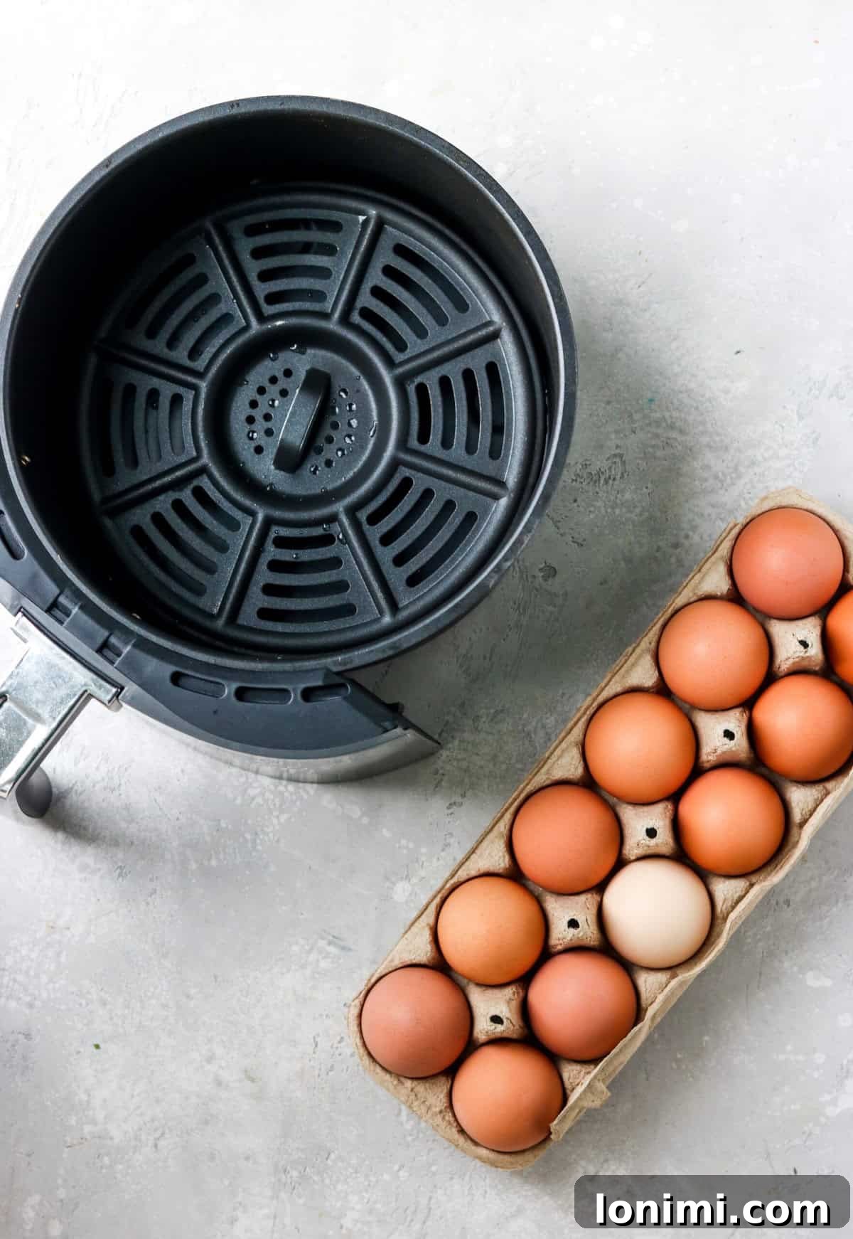 An empty air fryer basket ready for eggs, with an open carton of brown eggs beside it.
