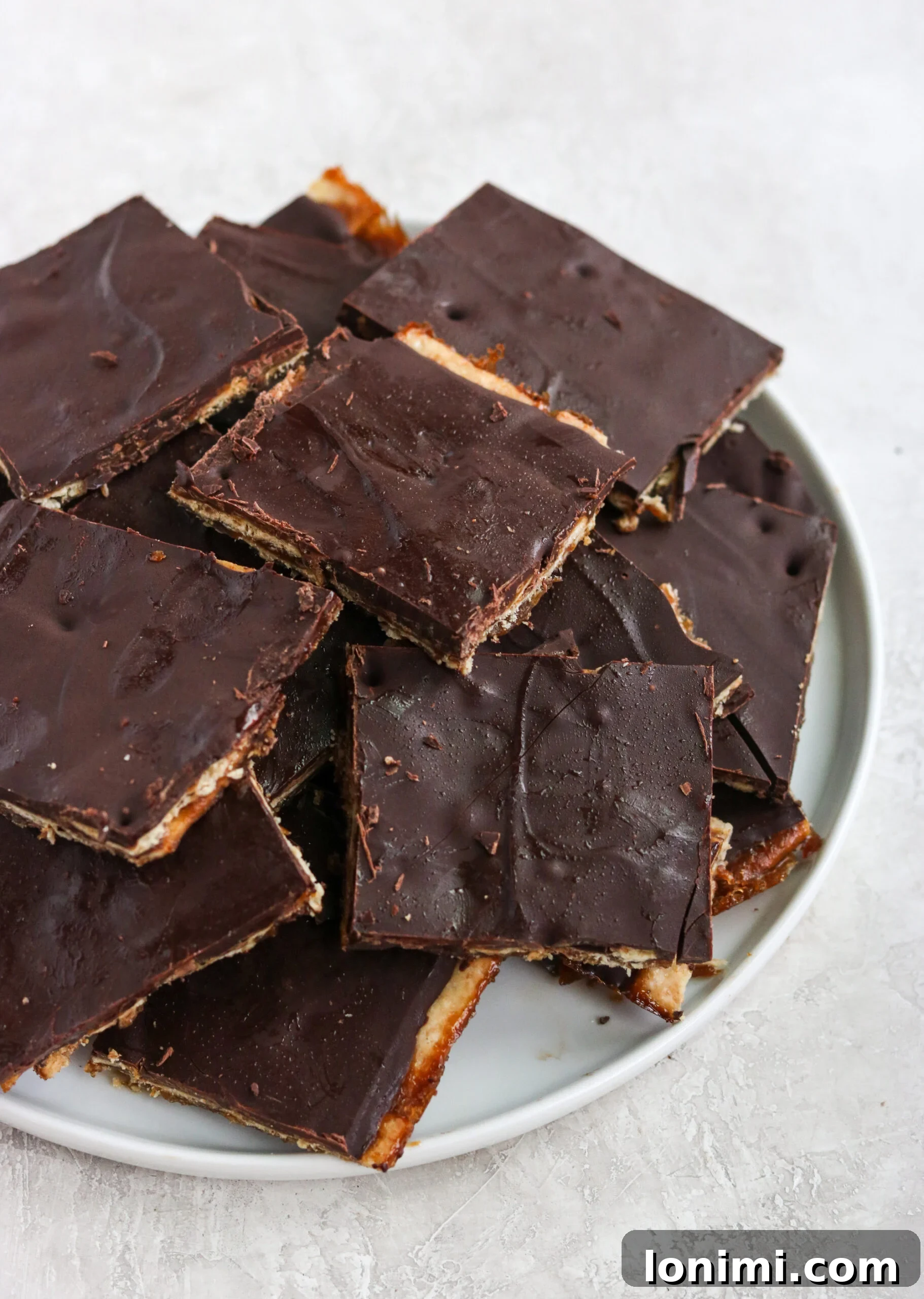 A plate brimming with freshly cut Paleo Christmas Crack bars, showcasing the distinct cracker, caramel, and chocolate layers.