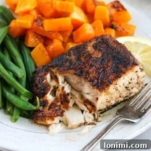 blackened mahi mahi on a plate with butternut squash and green beans with a fork flaking the fish apart