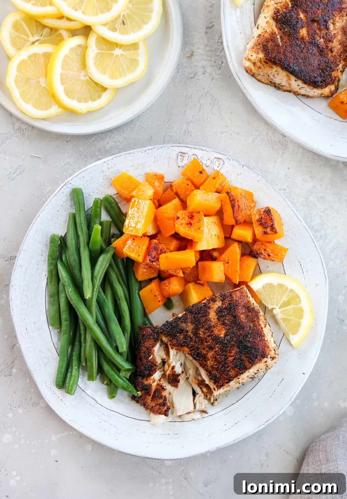 An inviting overhead shot of a white dinner plate artfully arranged with a generous serving of flaky, white blackened fish, accompanied by vibrant green beans and golden roasted sweet potatoes, creating a balanced and appealing meal.
