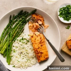 air fryer frozen salmon with honey garlic sauce and cauliflower rice and asparagus in a bowl with a fork flaking the fish