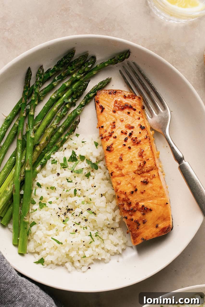a piece of air fryer salmon on a plate with white rice and asparagus.
