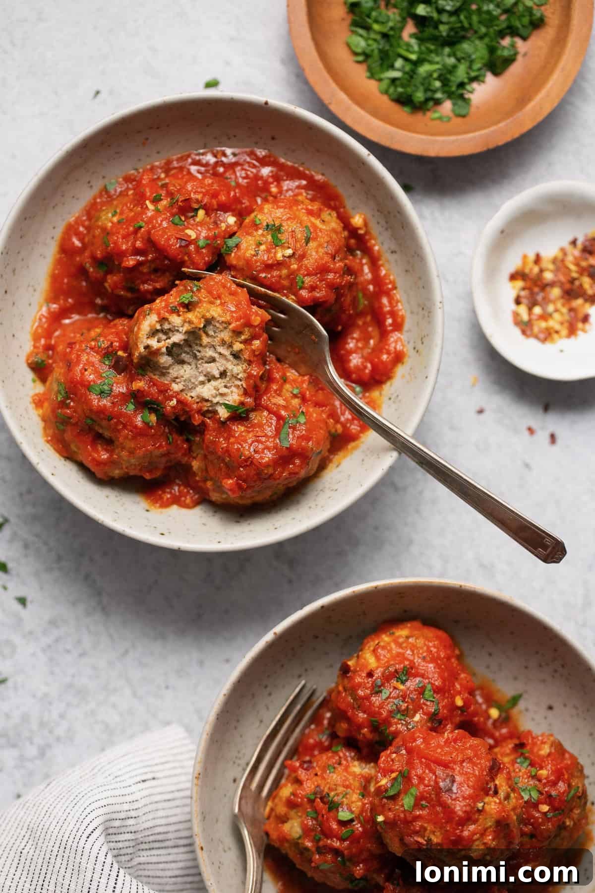 Gluten-free turkey meatballs served with sauce in two bowls, garnished with parsley and red pepper flakes
