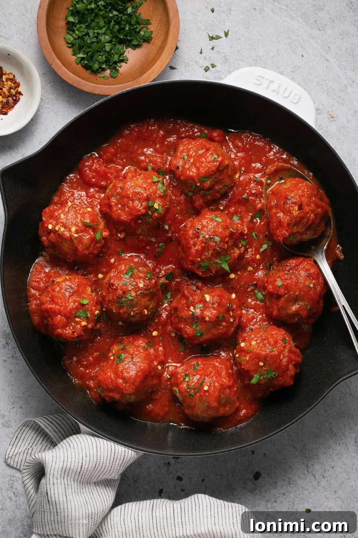 Gluten-free turkey meatballs with marinara sauce in a white and black cast iron skillet, garnished with fresh parsley