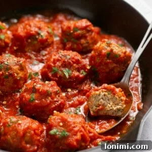 Air fryer turkey meatballs in a cast iron skillet with marinara sauce and a spoon scooping one out