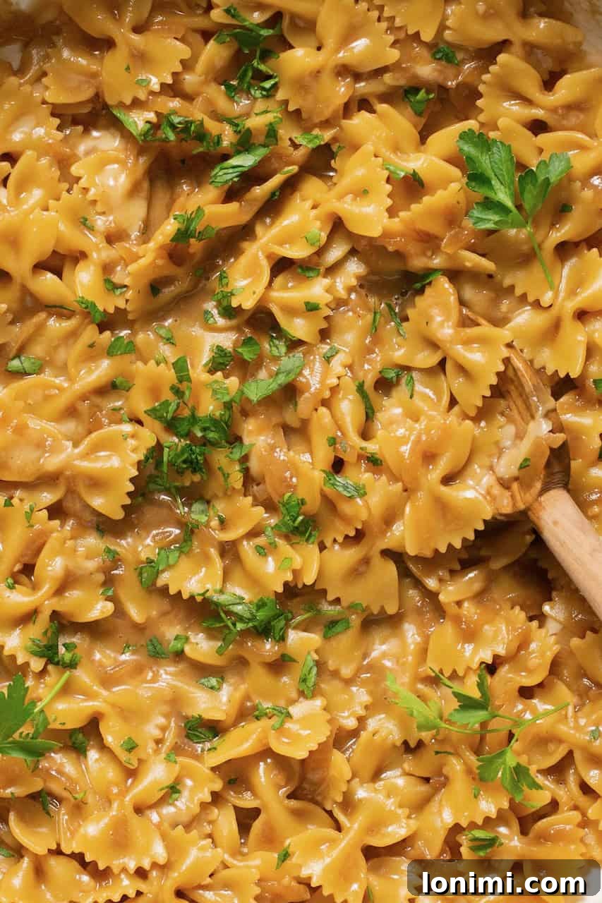 Gluten Free French Onion Pasta The TikTok Sensation 6 An up-close overhead shot of cooked French onion pasta being stirred with a wooden spoon in a pot, showcasing its creamy texture.