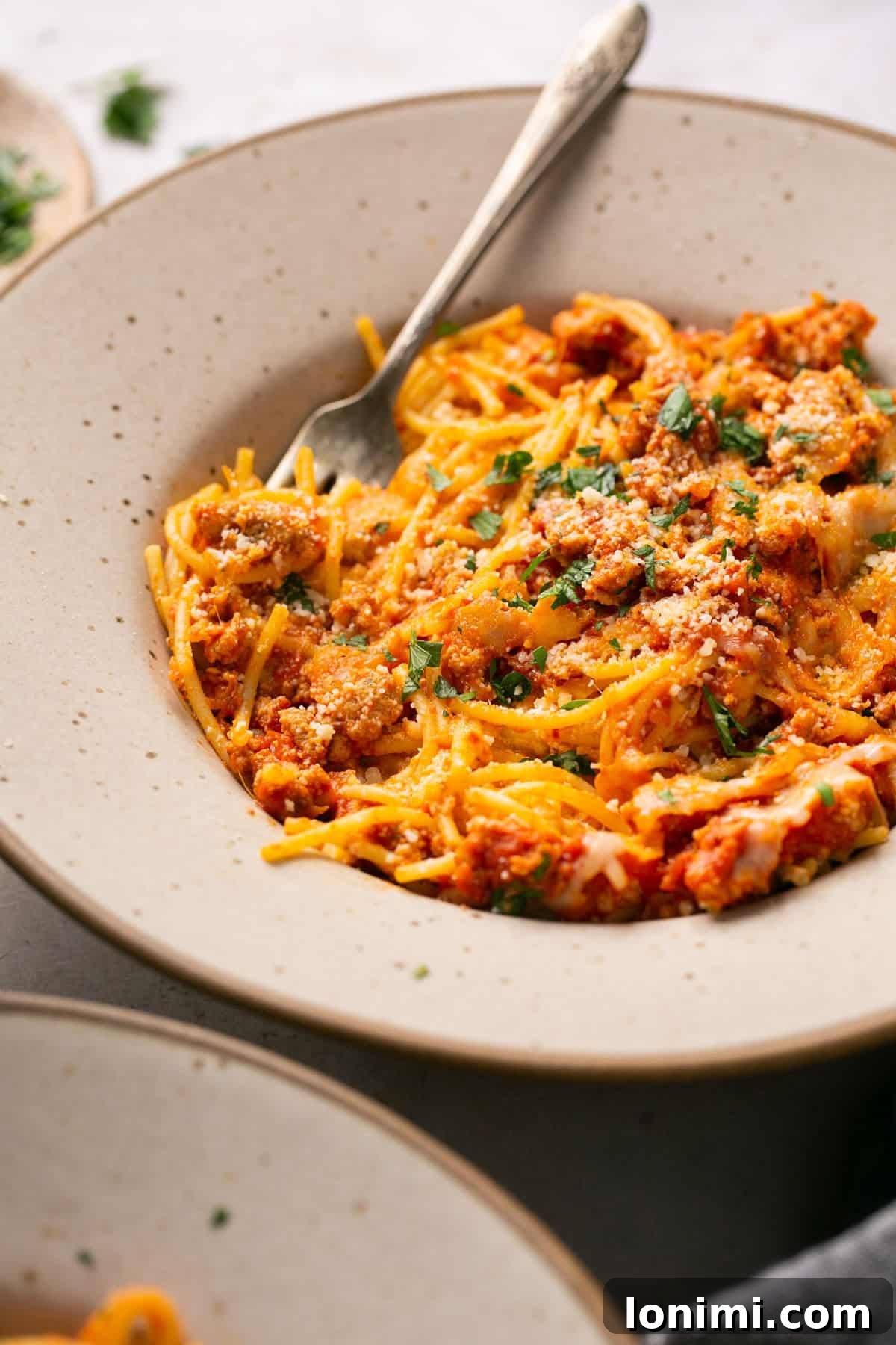 A plate with a generous serving of baked spaghetti alfredo, garnished with fresh chopped basil and grated parmesan cheese.