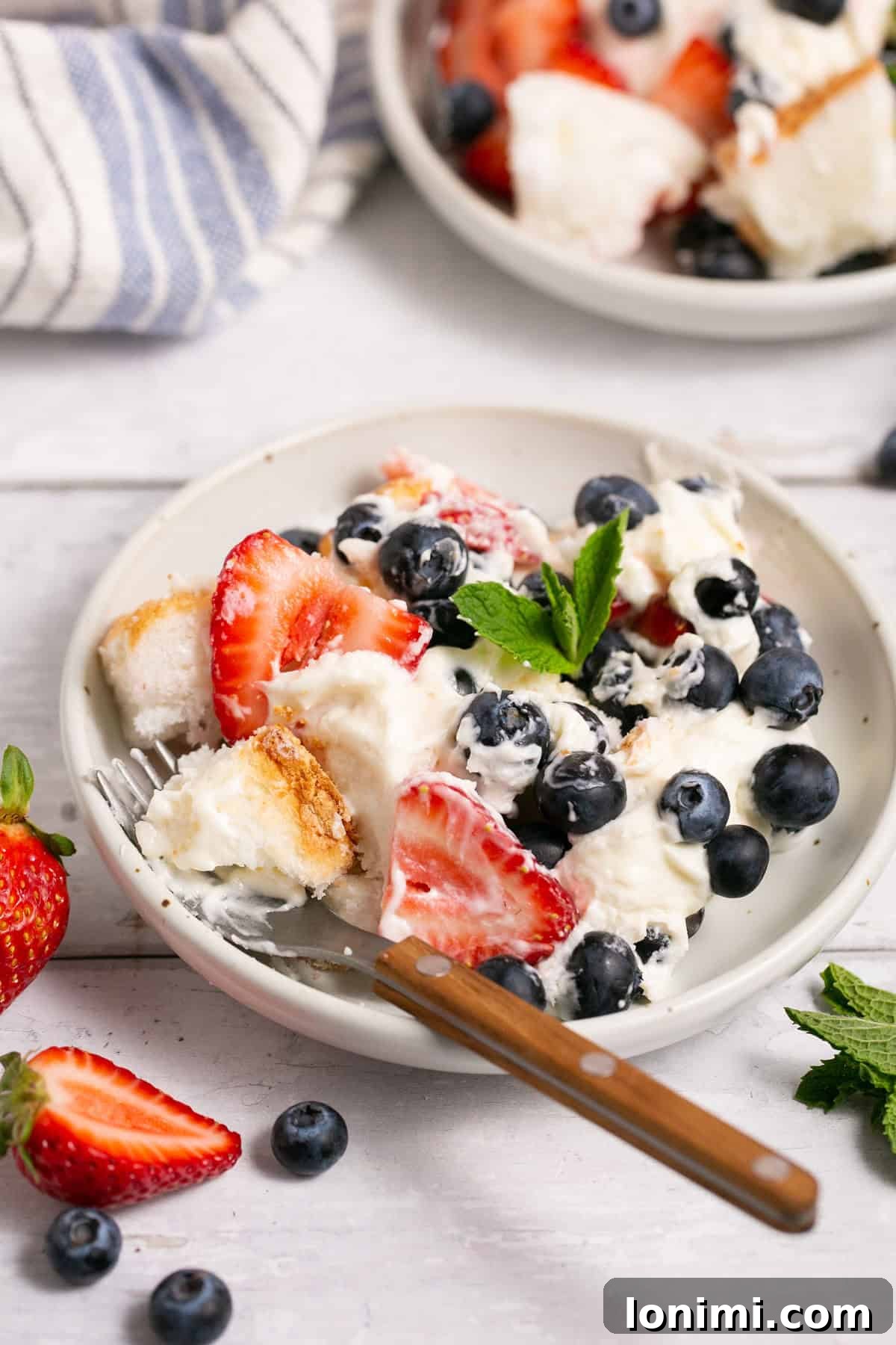 Heavenly Gluten-Free Strawberry Angel Food Trifle 8 A close-up shot of a gluten-free berry angel food cake trifle in a glass bowl with a serving spoon, highlighting the delicious layers of cake, fruit, and cream.