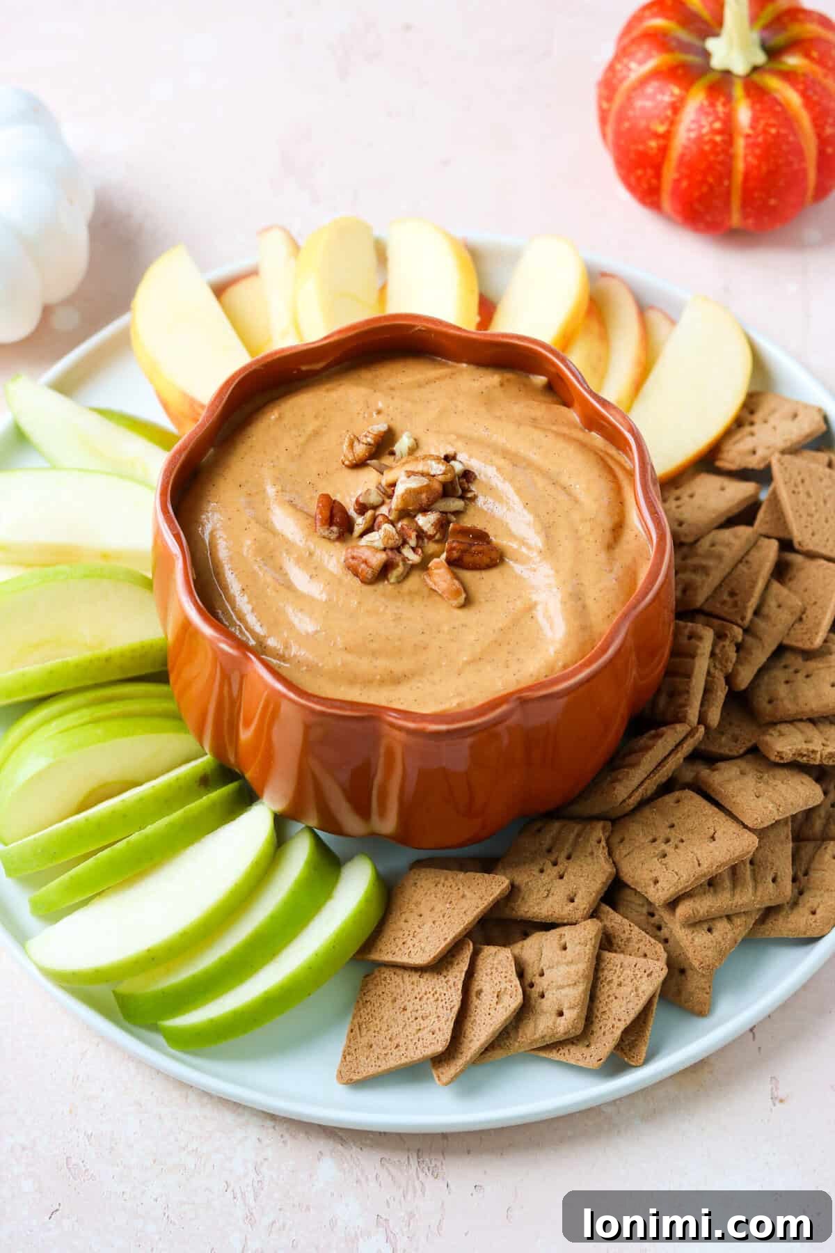 A beautifully presented pumpkin cream cheese dip in a pumpkin-shaped bowl, surrounded by fresh apple slices and gluten-free sweet thins, ready for a fall gathering.