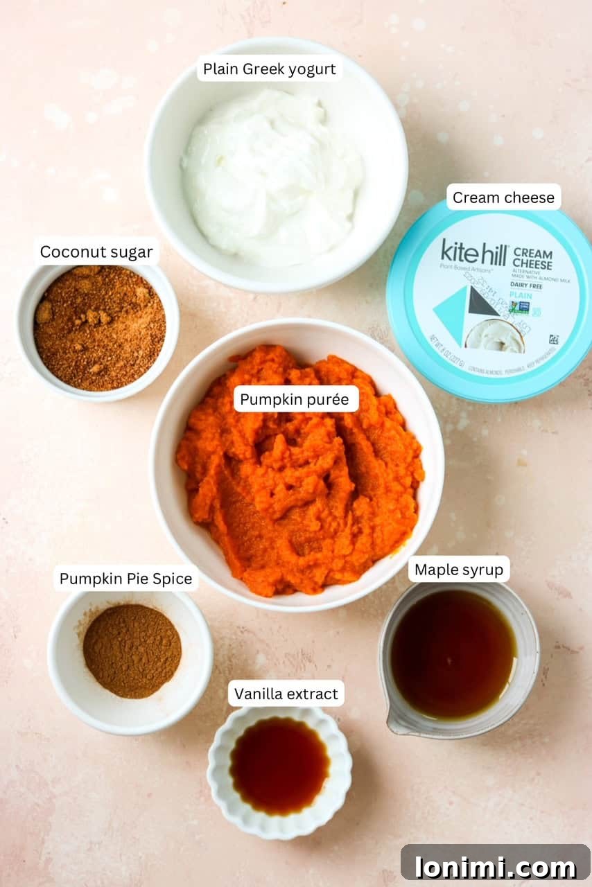 All the essential ingredients for a healthy pumpkin cream cheese dip laid out on a clean surface, including canned pumpkin puree, cream cheese, Greek yogurt, maple syrup, pumpkin pie spice, coconut sugar, and vanilla extract.