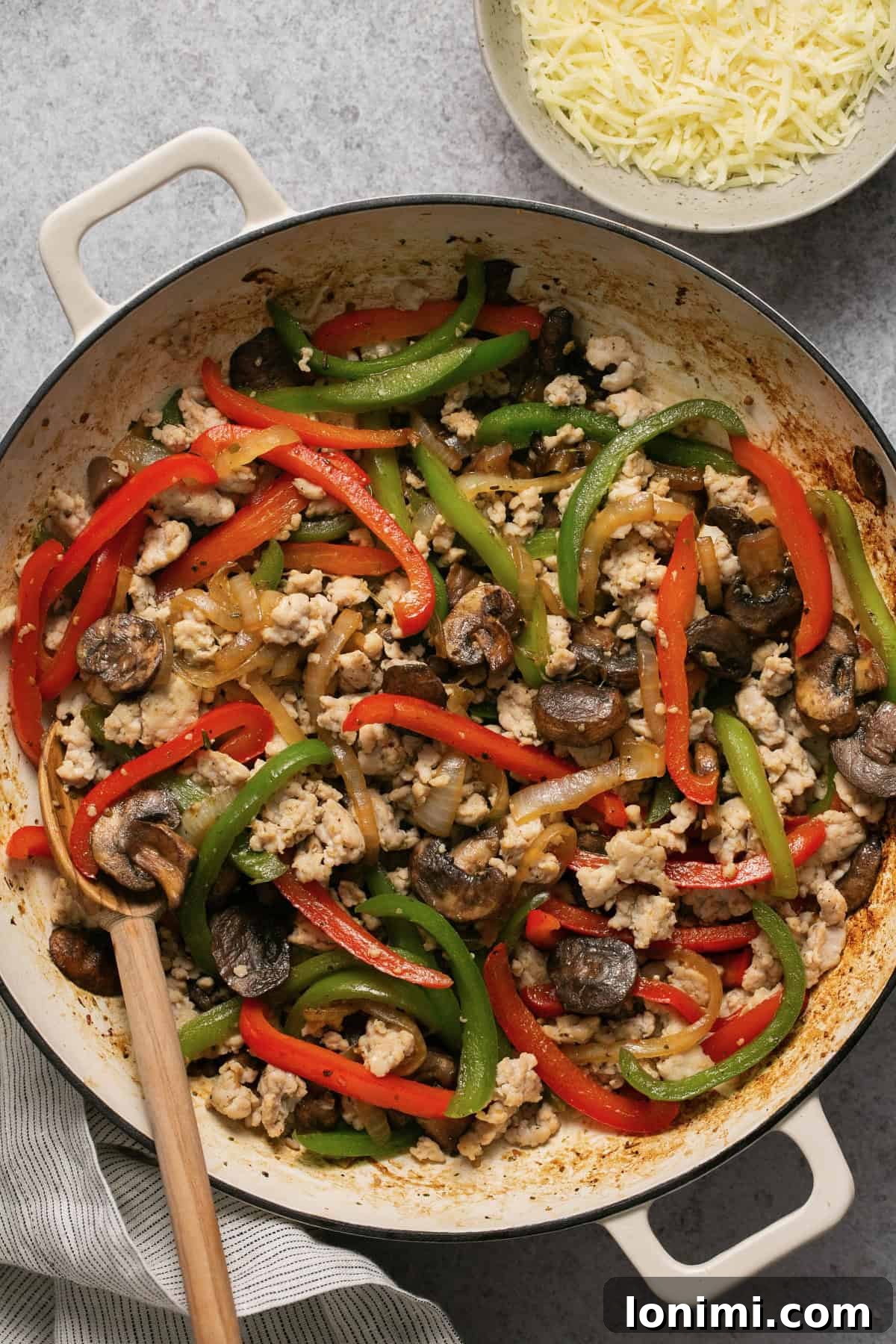 ground chicken with peppers, onions and mushrooms in a skillet with cheese on the side