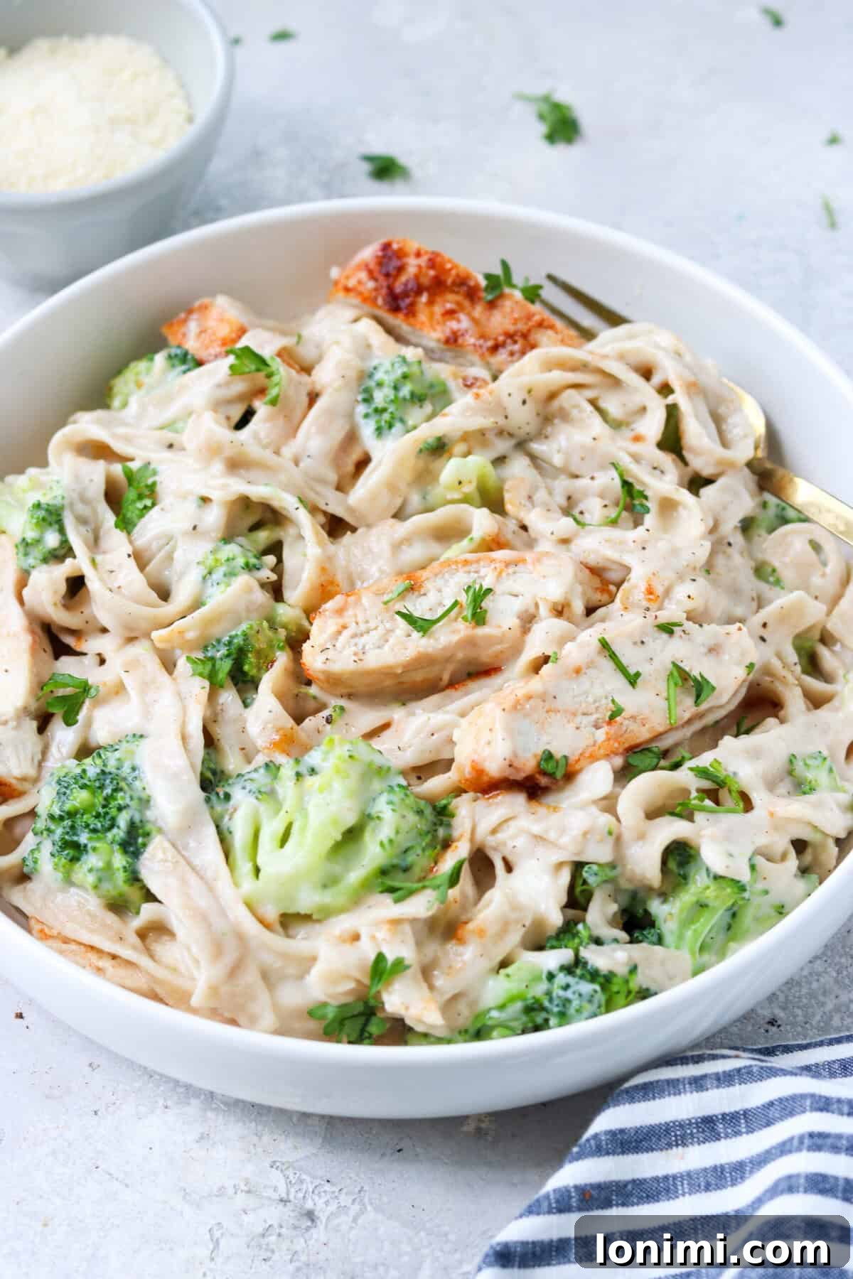 chicken and broccoli with alfredo sauce mixed with gluten free tagliatelle in a bowl topped with parsley