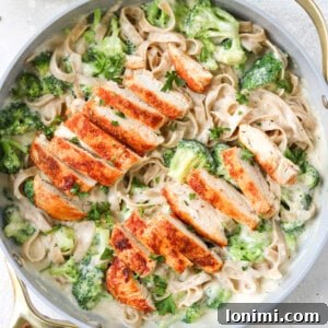 chicken and broccoli with alfredo sauce and gluten free pasta in a skillet with a napkin and a small bowl of parmesan on the side