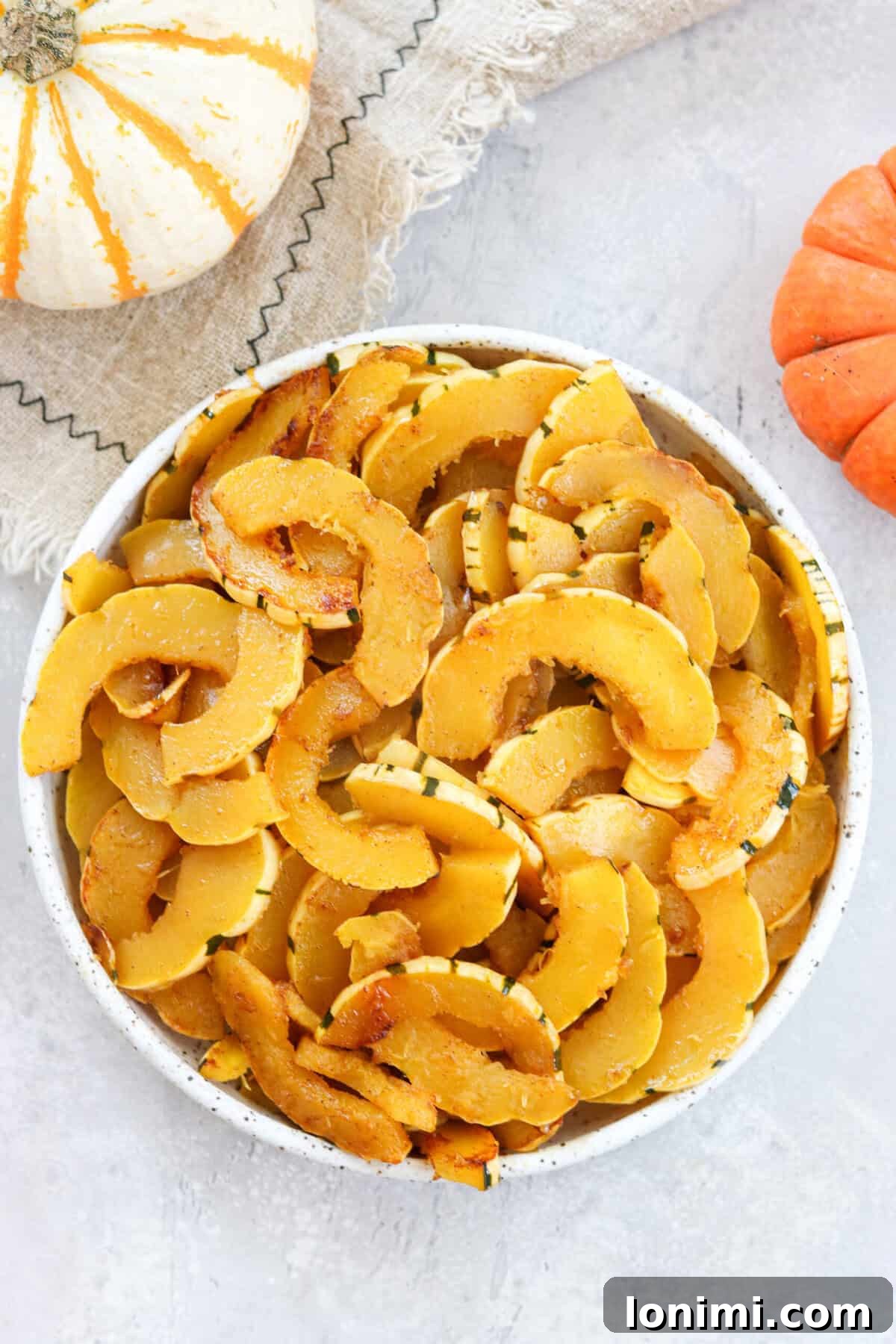 Beautifully sautéed delicata squash served in a bowl, surrounded by autumnal pumpkins and decor, ready to be enjoyed.