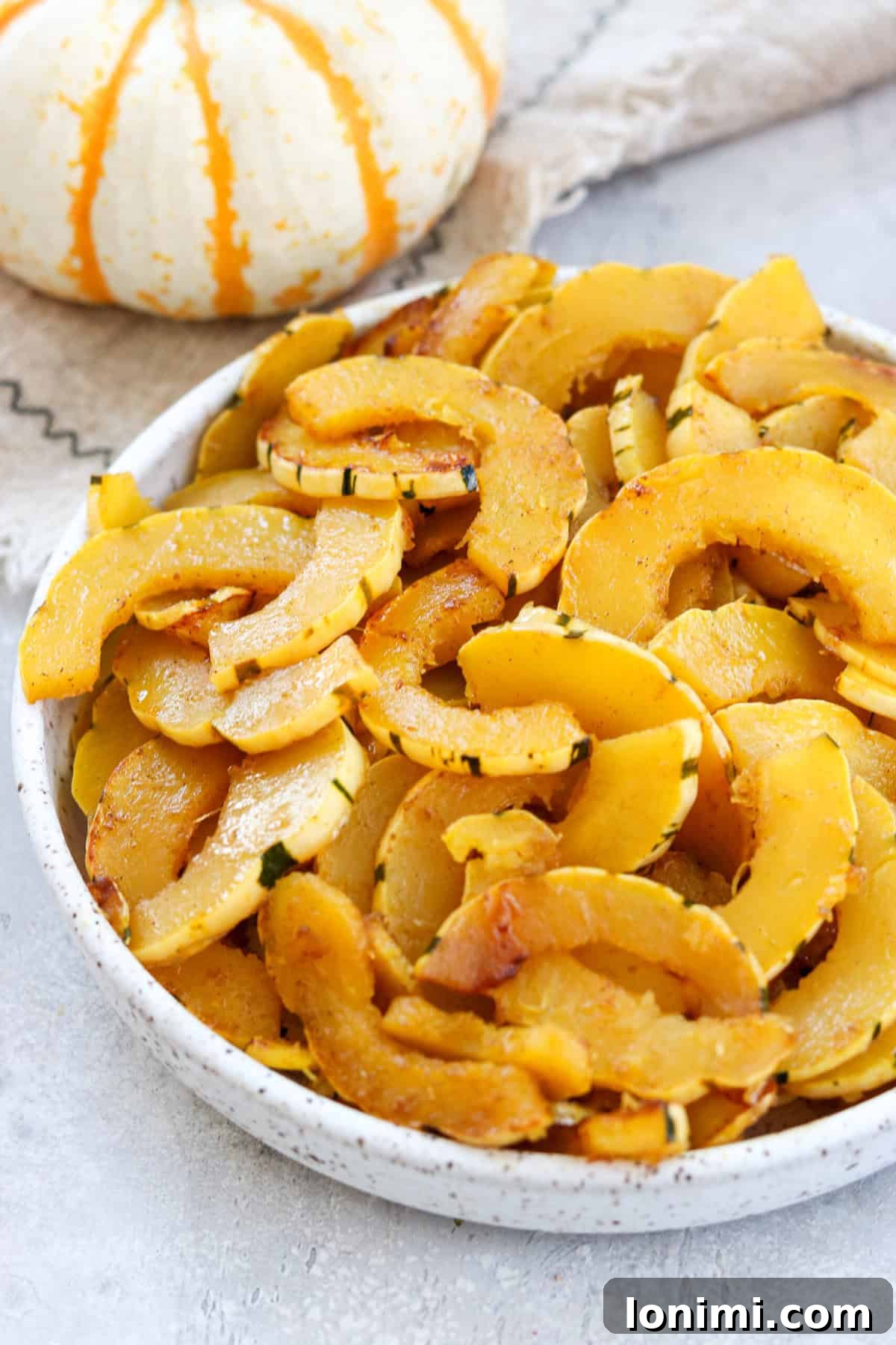 A close-up of sautéed delicata squash sprinkled with cinnamon in a rustic bowl, next to a small pumpkin, highlighting the warm, inviting fall theme.