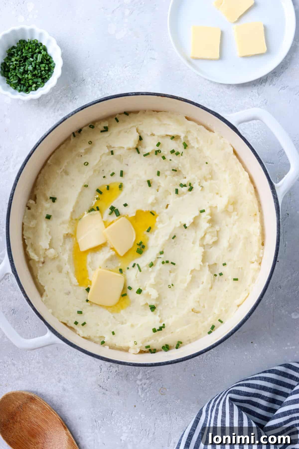 Gluten-free mashed potatoes in a cooking pot, topped with fresh chives and a melting pat of butter