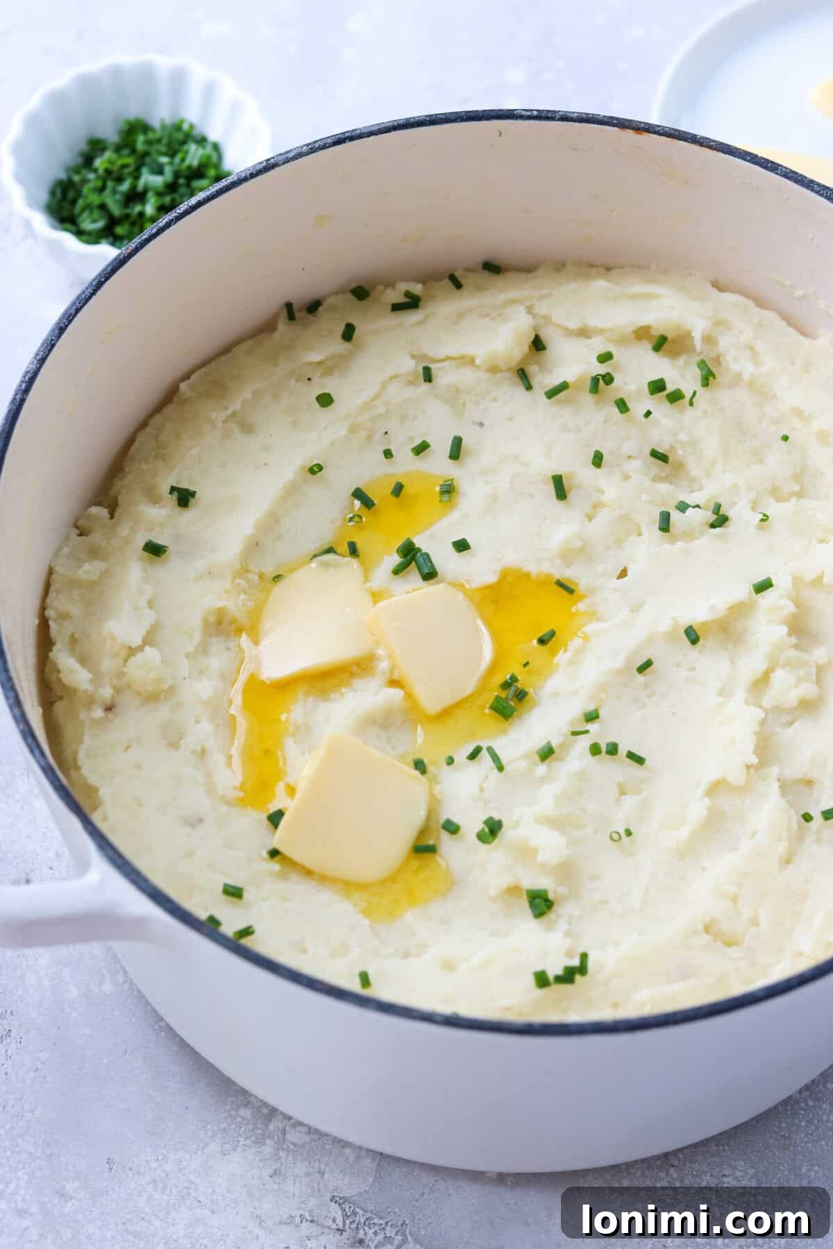 A side view of creamy gluten-free mashed potatoes in a cooking pot, garnished with chives and melting butter