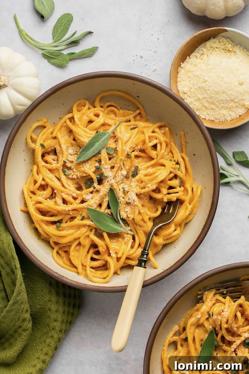 Velvety Pumpkin Pasta 2 Two bowls of pumpkin pasta topped with grated parmesan cheese and fresh sage, with a fork in one bowl, ready to eat.
