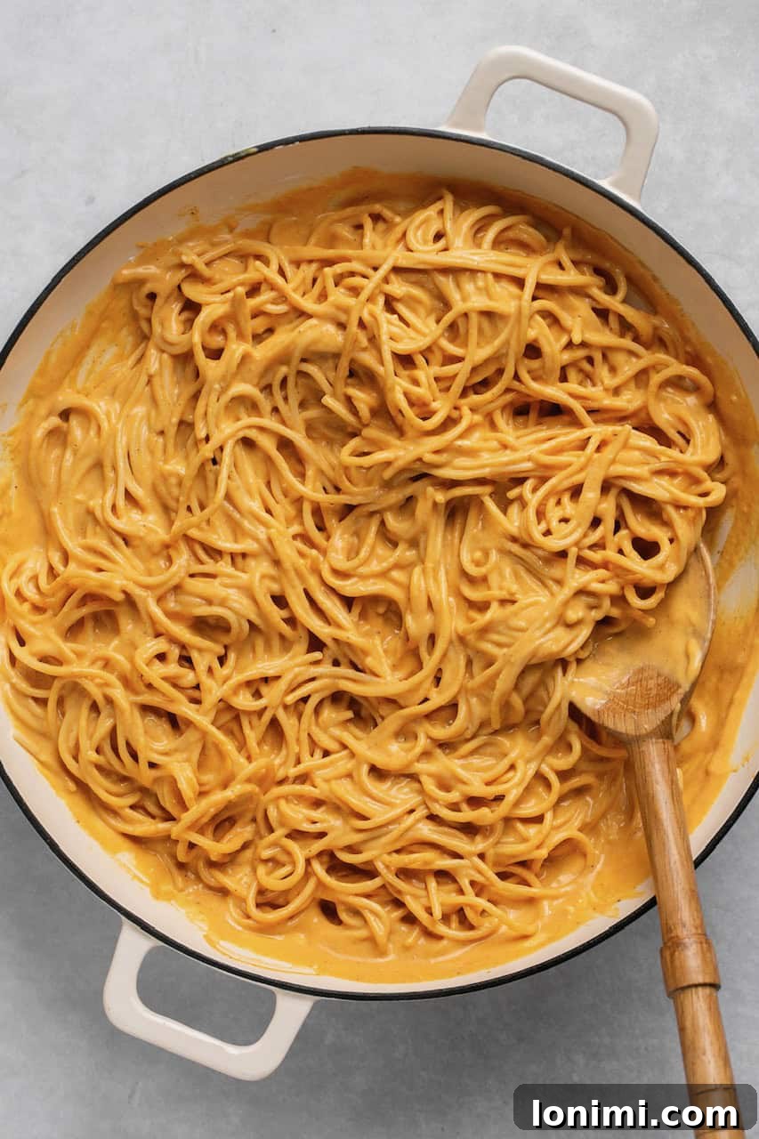 Velvety Pumpkin Pasta 6 A pot of gluten-free spaghetti coated in creamy pumpkin sauce, with a wooden spoon resting inside, ready to be served.