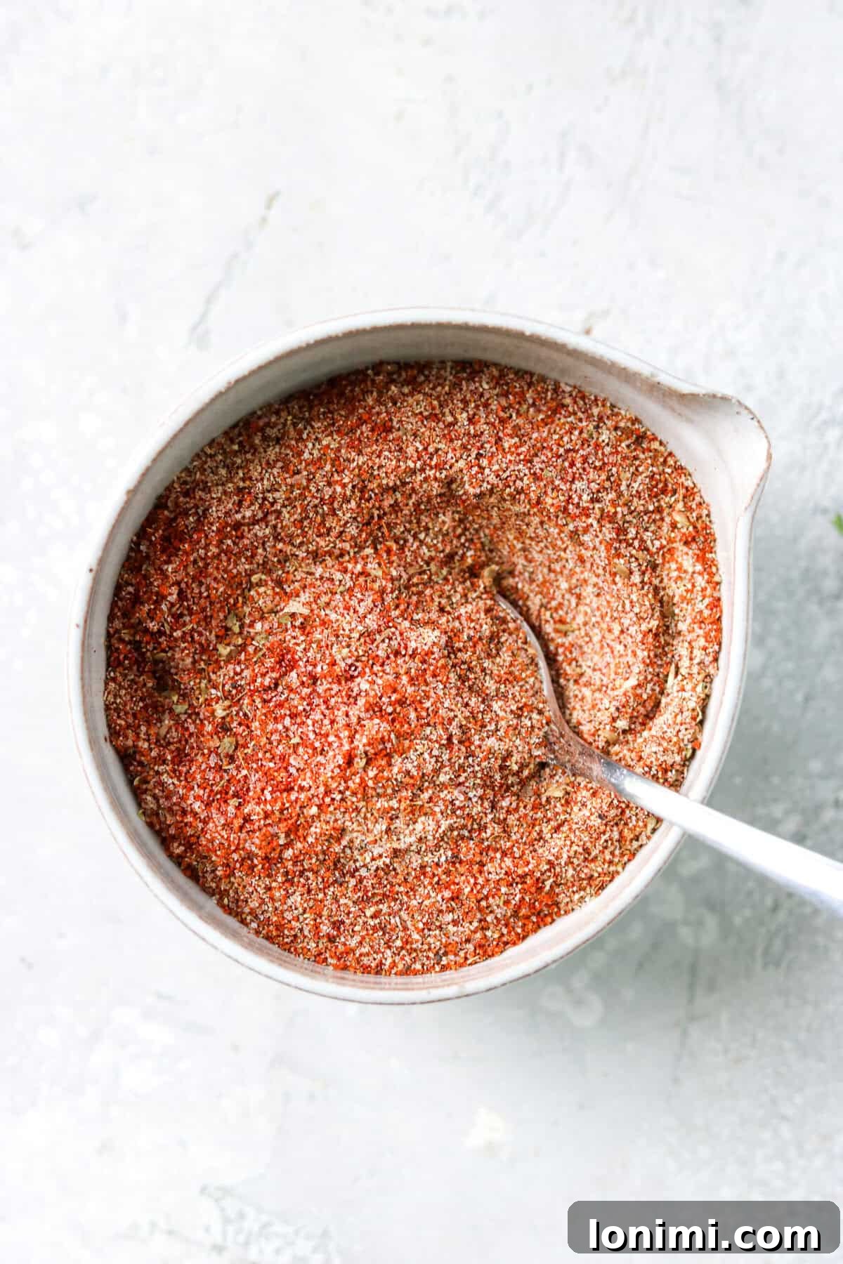 A wooden bowl filled with freshly mixed chicken taco seasoning, with a small silver spoon scooping some out, highlighting the rich color and texture.