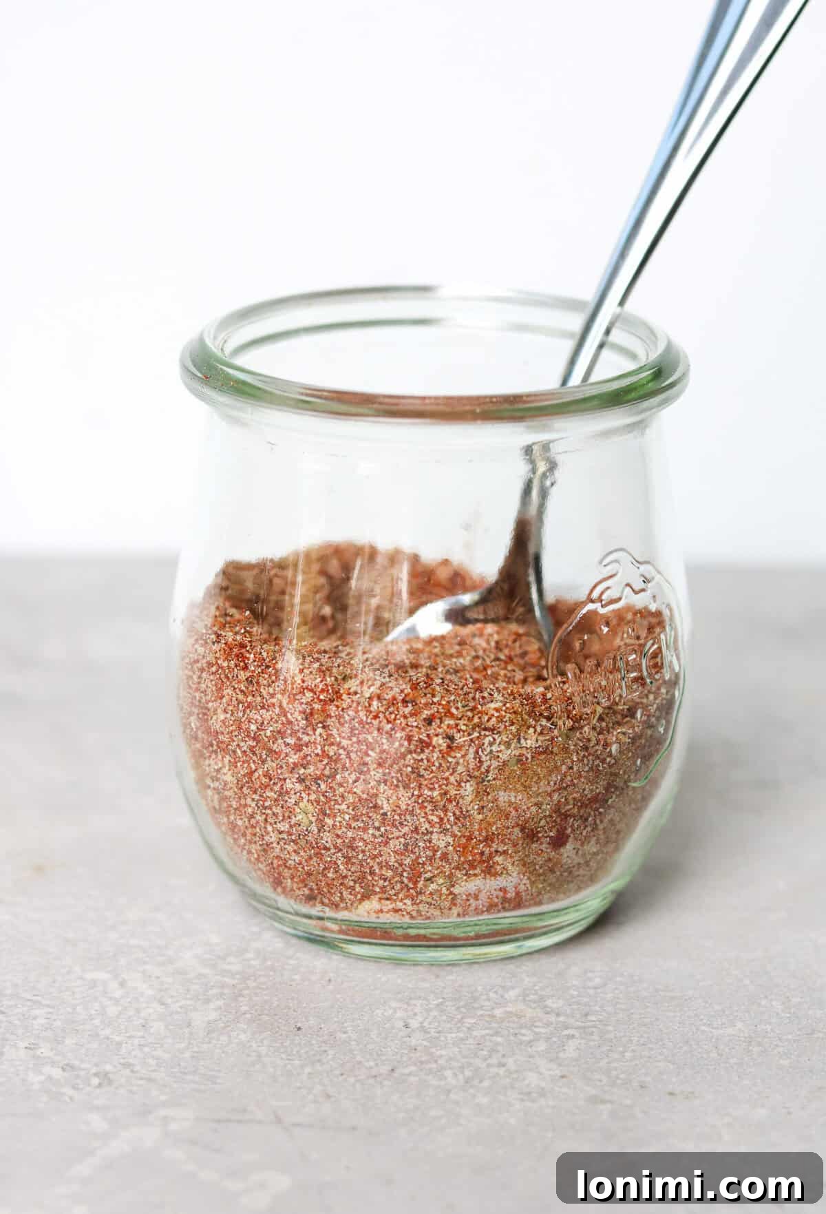 A tightly sealed glass jar of homemade taco seasoning with a small measuring spoon, ready for storage in a pantry.