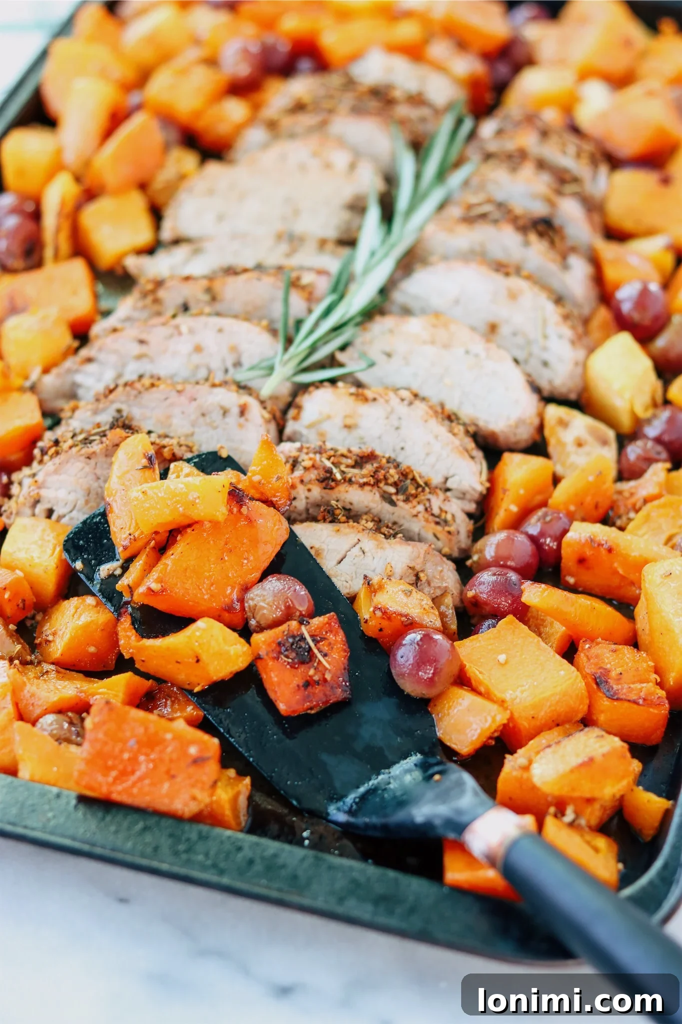 Perfectly roasted pork tenderloin with butternut squash and grapes on a sheet pan, ready to serve.