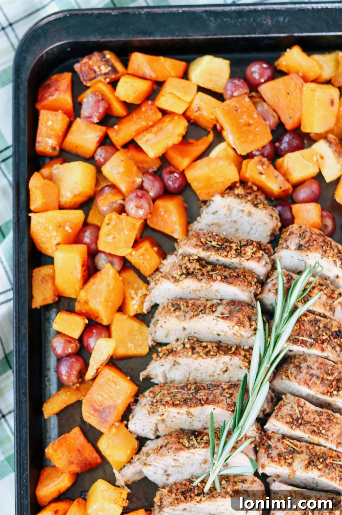 Close-up of seasoned pork tenderloin and cubed butternut squash on a baking sheet before roasting.