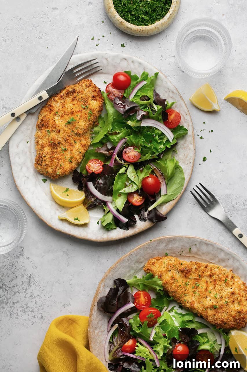air fryer chicken cutlets on 2 plates with a side salad and lemon slices 