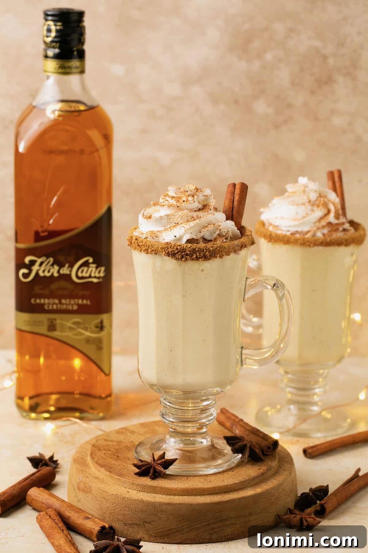 A glass of dairy-free eggnog with whipped cream and a bottle of Flor de Caña rum in the soft-focus background.