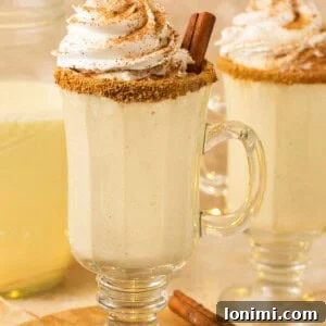A festive glass of dairy-free eggnog, crowned with whipped cream and a cinnamon stick, capturing the spirit of the holidays.