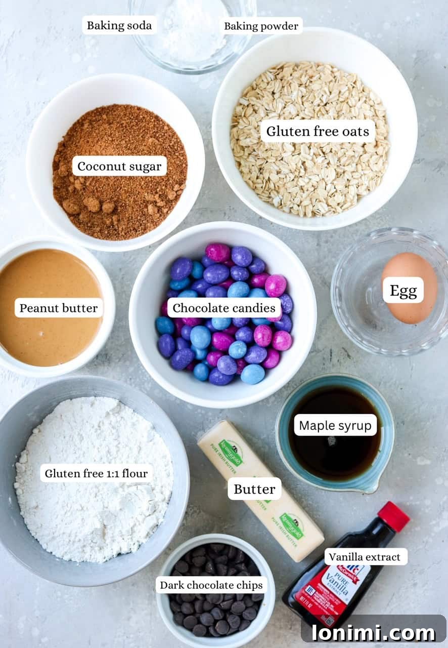 A vibrant flat lay of all the essential ingredients laid out neatly for making gluten free monster cookies. Includes butter, eggs, coconut sugar, maple syrup, peanut butter, gluten-free flour, gluten-free oats, colorful chocolate candies, and dark chocolate chips.