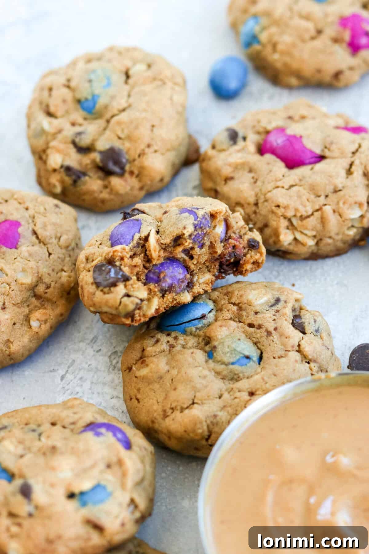 A close-up of a gluten free monster cookie with a bite taken out, revealing its soft, chewy interior and a rich assortment of chocolate candies and dark chocolate chips. The focus is on the inviting texture and delicious fillings.