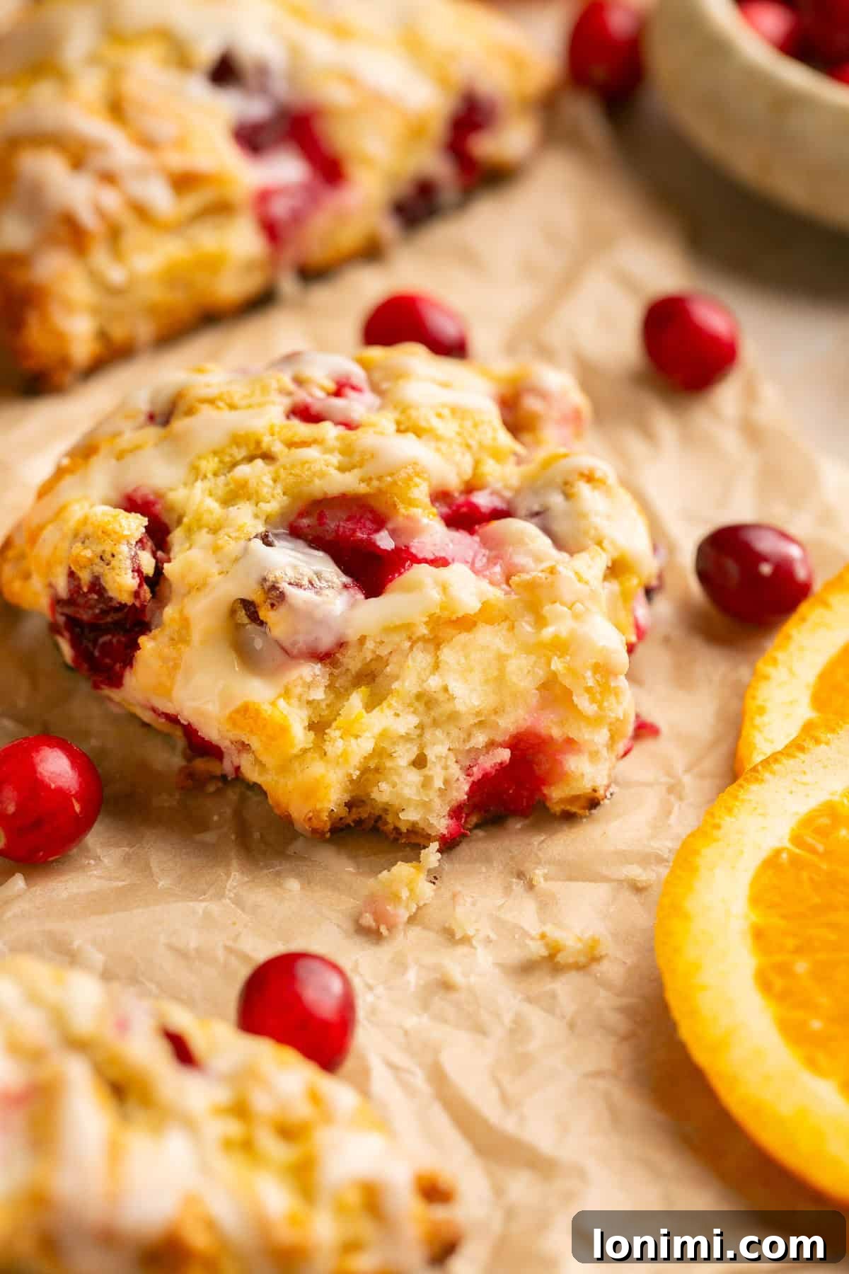A single gluten-free orange cranberry scone on parchment paper with a bite taken out, showing its flaky interior.