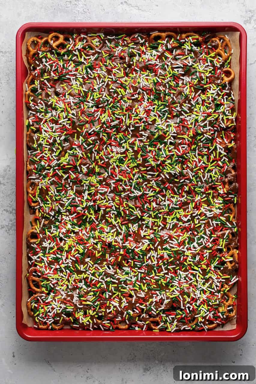 Addictive Gluten-Free Holiday Pretzel Bark 6 A large pan of freshly made caramel and chocolate-covered pretzels, generously topped with festive sprinkles, ready to be chilled and broken into pieces.