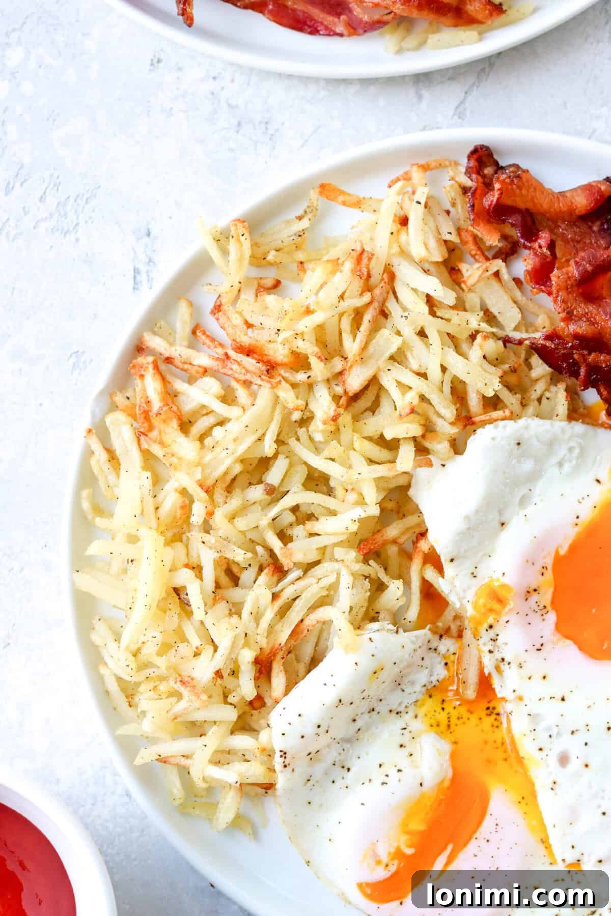 a close up of cooked hash browns on a plate with eggs and bacon