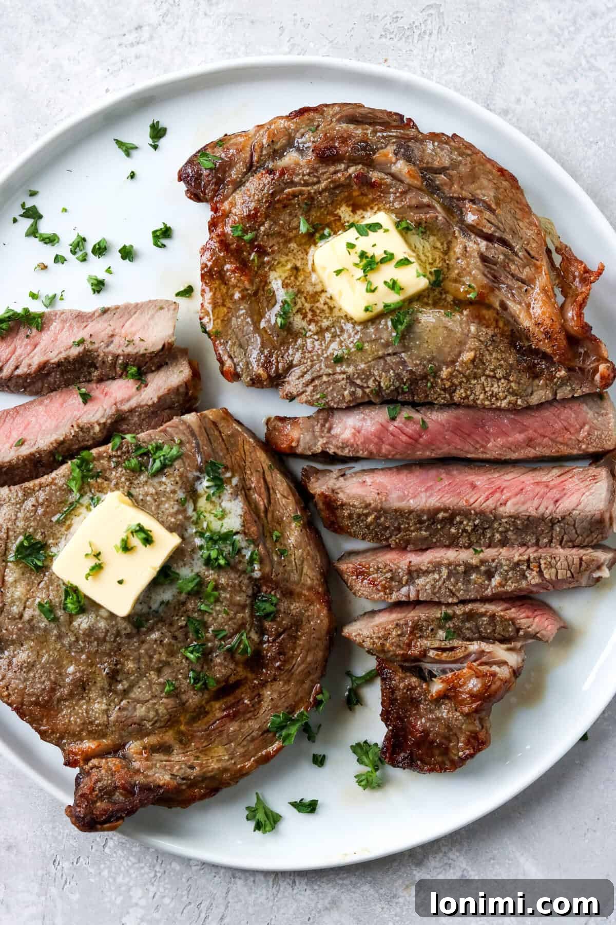 sliced ribeye steak on a white plate topped with butter and parsley