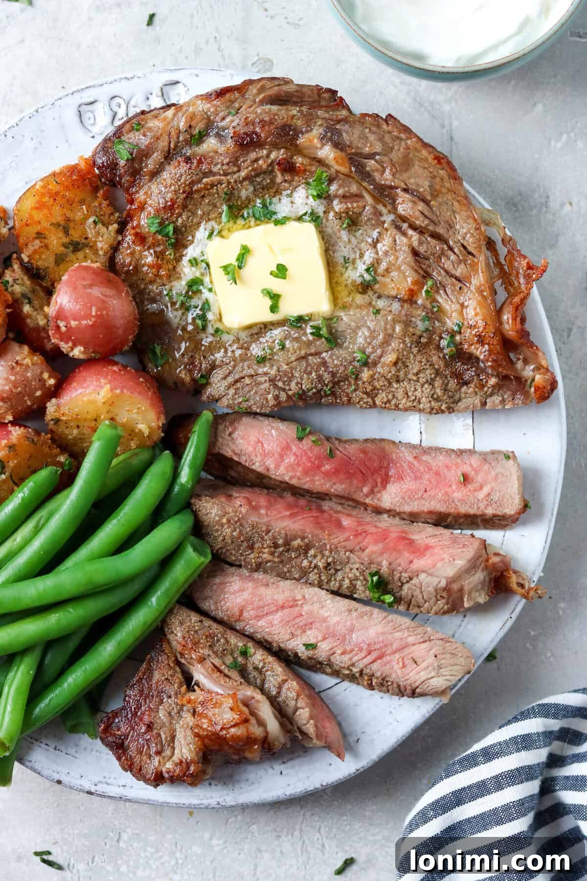 sliced ribeye steak topped with butter and parsley with green beans and potatoes on the side