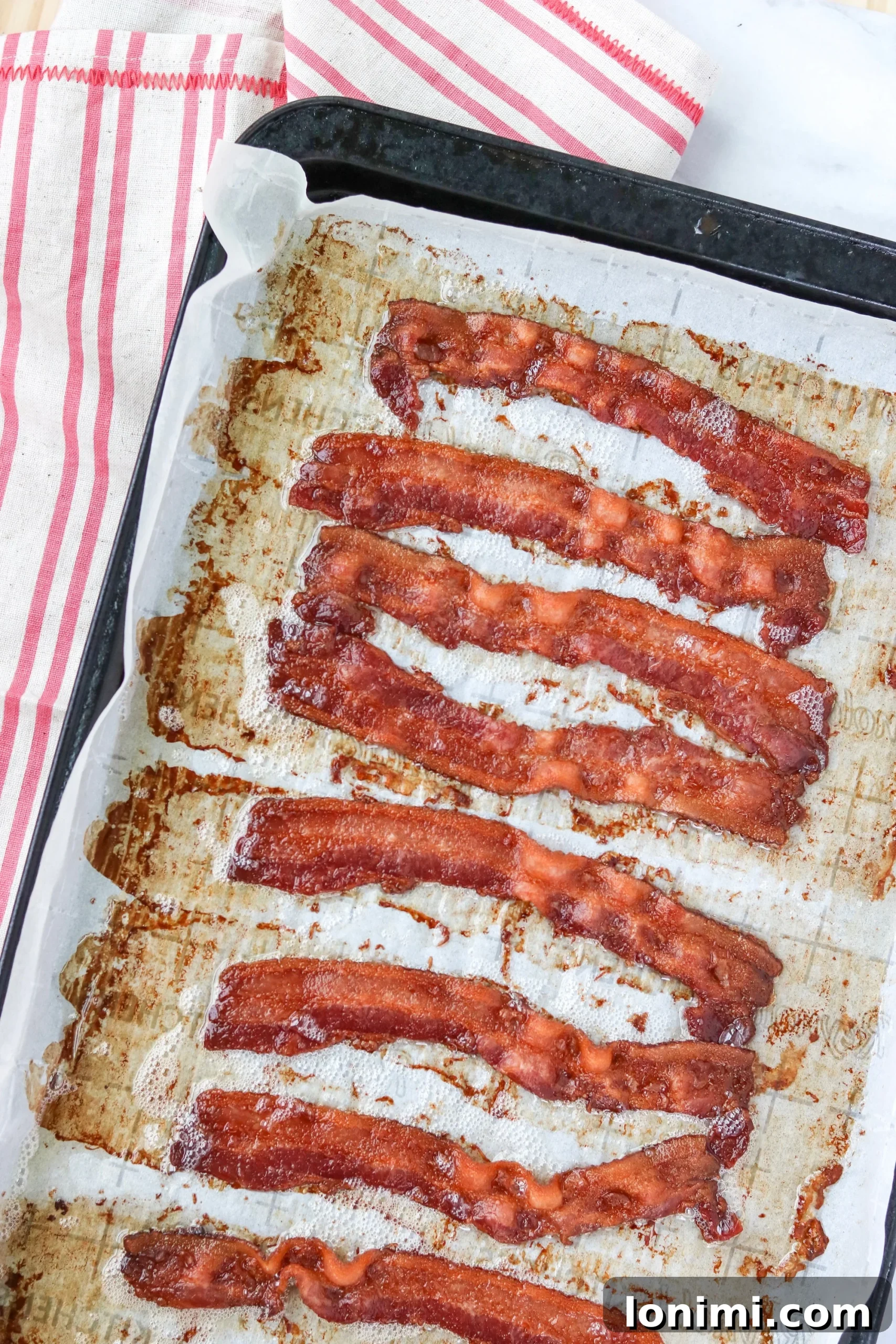 Effortless Crispy Baked Bacon 3 Two strips of raw bacon laid on a parchment paper-lined baking sheet, ready for the oven.