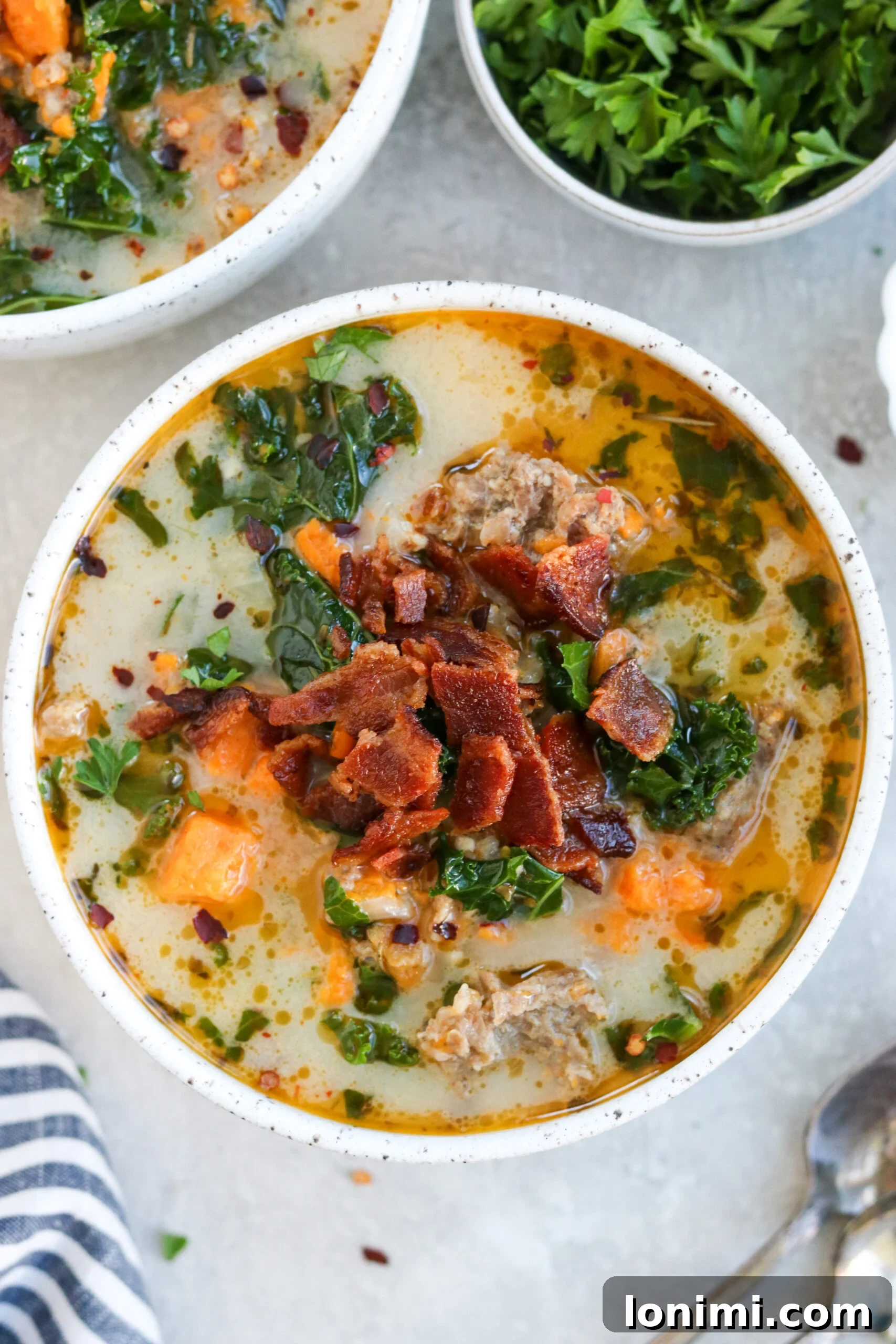 Hearty Whole30 Paleo Gluten Free Zuppa Toscana 2 A steaming bowl of Whole30 Zuppa Toscana garnished with crispy bacon and fresh parsley