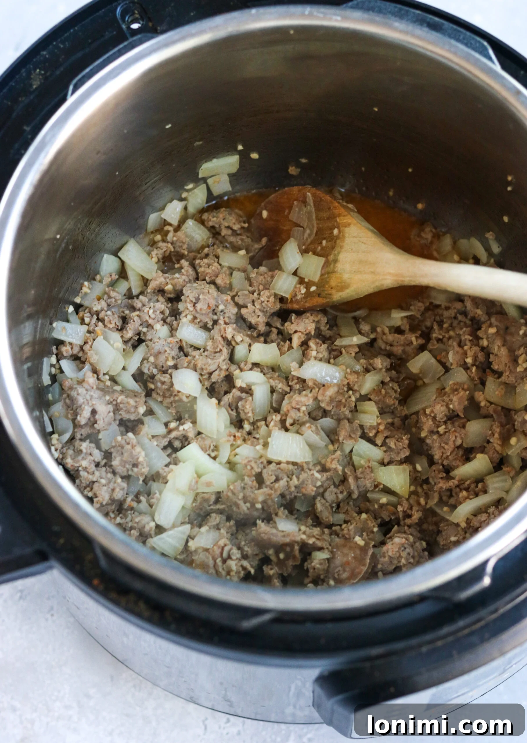 Hearty Whole30 Paleo Gluten Free Zuppa Toscana 4 Sautéed Italian sausage, onions, and garlic cooking together in an Instant Pot, forming a fragrant base for the soup