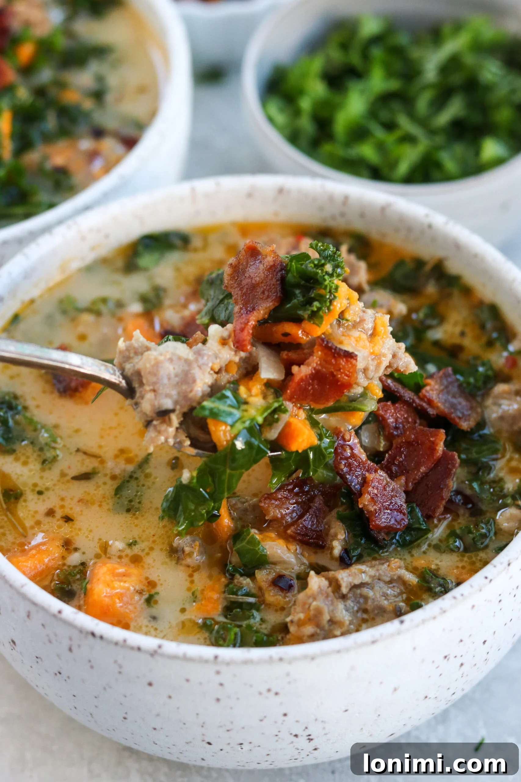 Hearty Whole30 Paleo Gluten Free Zuppa Toscana 7 A close-up of a spoonful of Whole30 Zuppa Toscana, showcasing the savory sausage, tender sweet potatoes, and crispy bacon topping