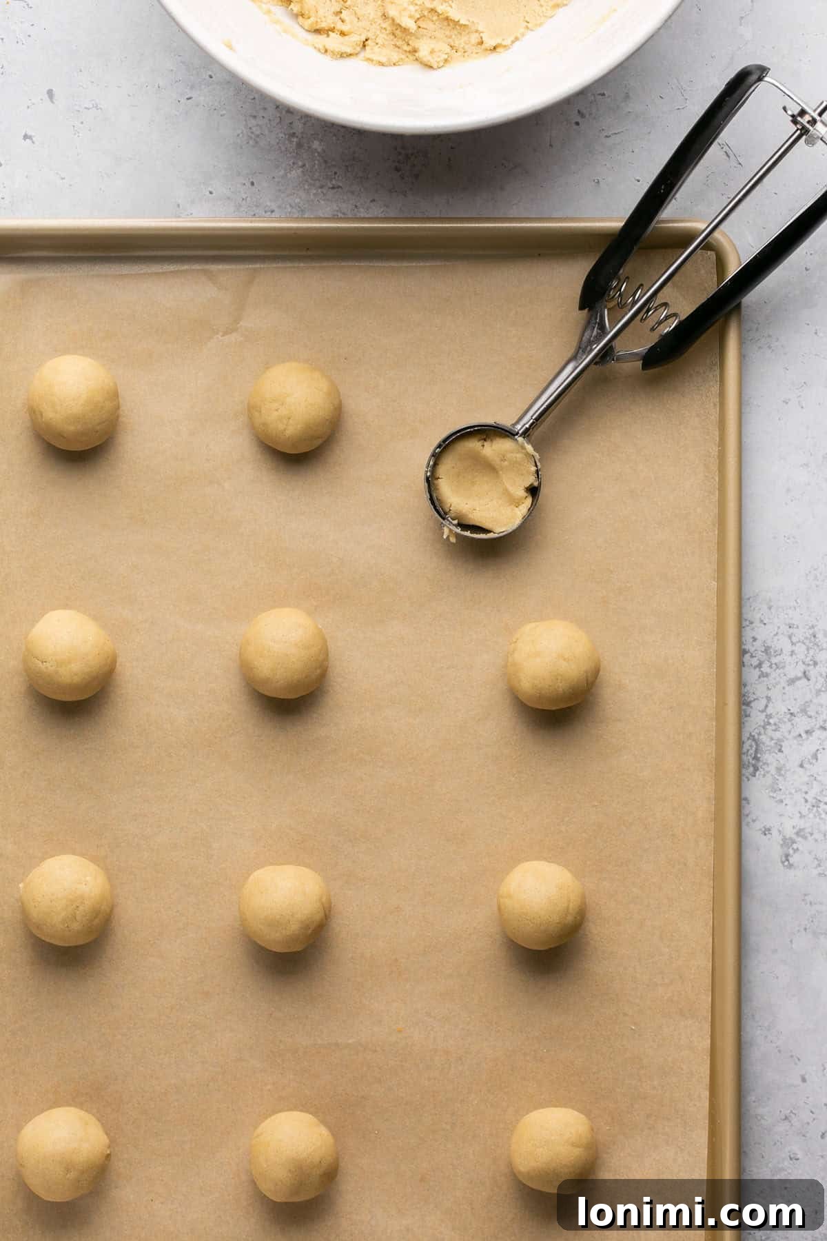 Balls of cookie dough evenly spaced on a parchment-lined baking sheet, with a cookie scoop nearby.