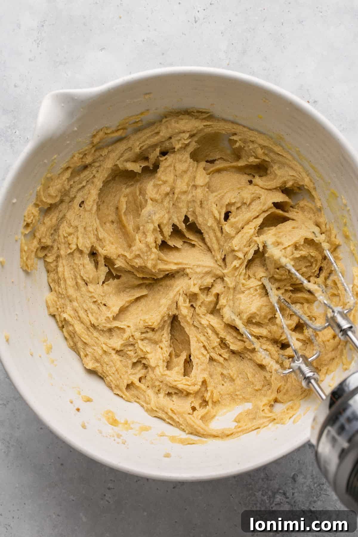 Well-combined mixture of eggs, sugars, and butter in a white mixing bowl.